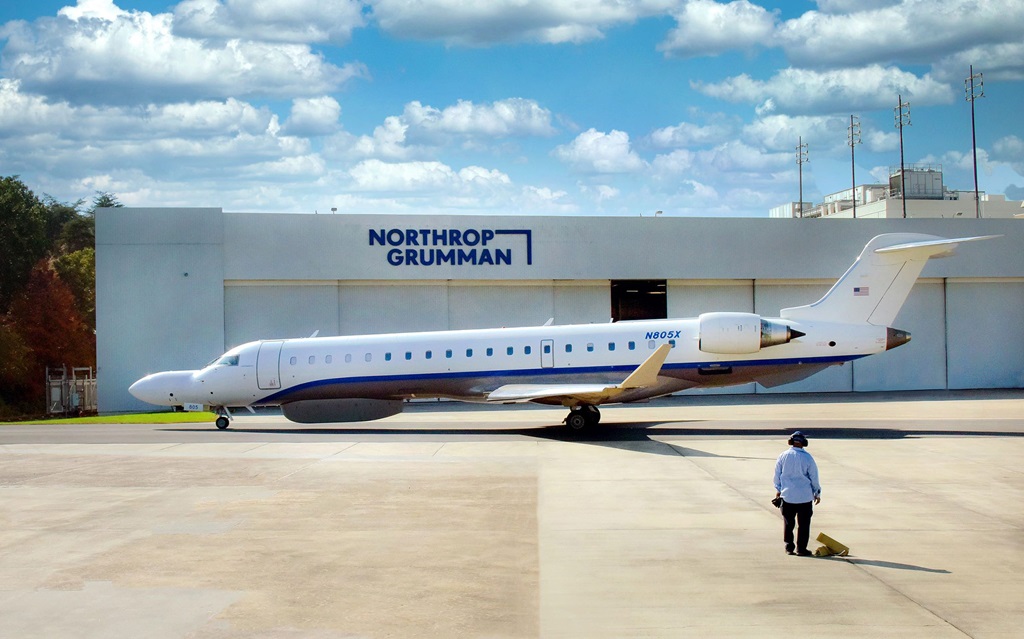 An aircraft sits on a runway in front of a Northrop Grumman hangar.