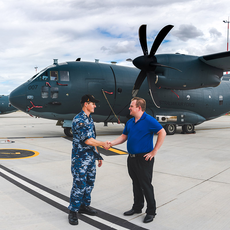 two white men shaking hands in front of airplane