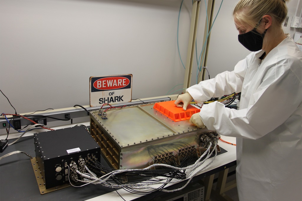 A white woman in a white lab coat test a hardware system