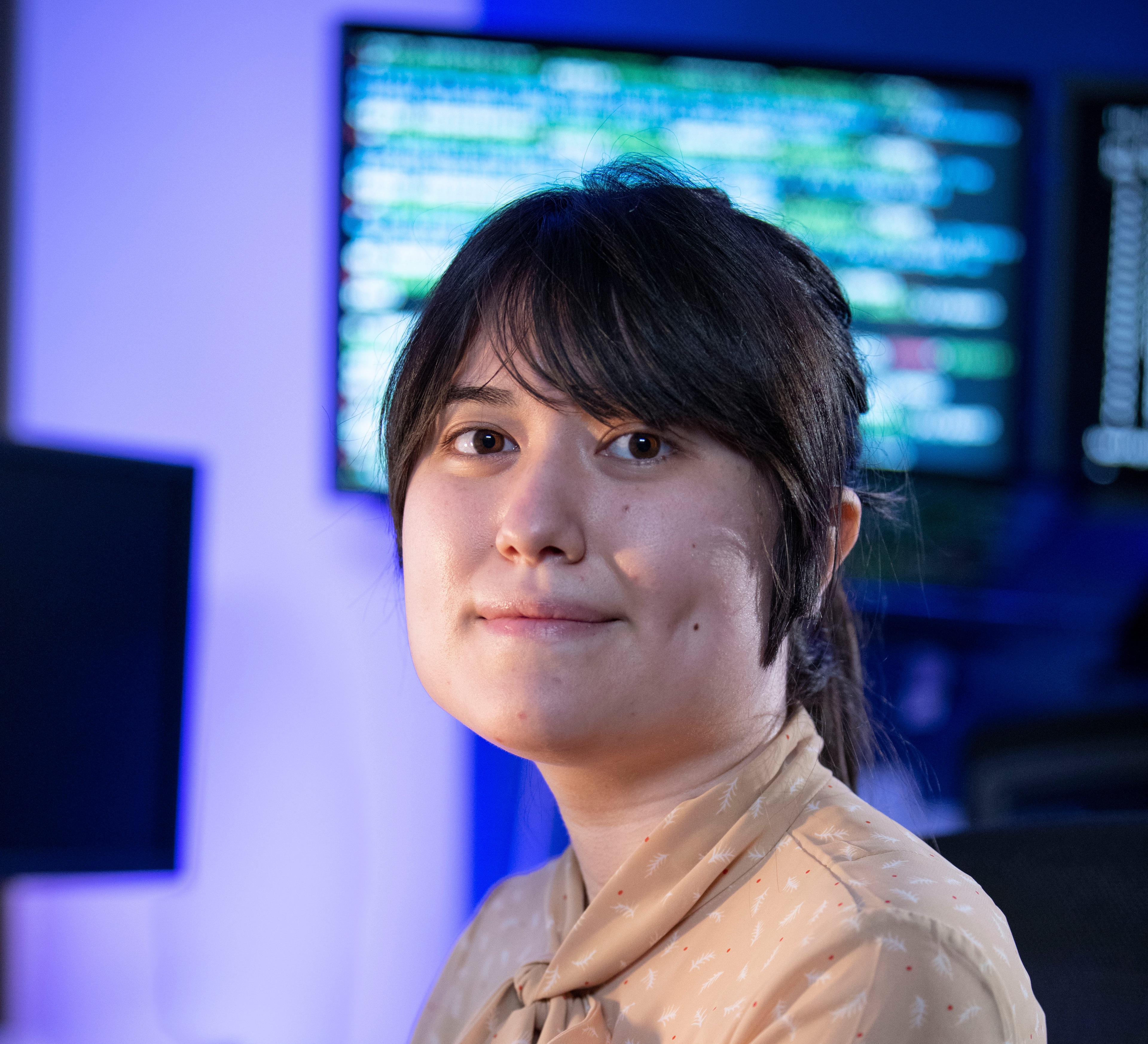 a woman looks directly at the camera with a computer monitor in the background