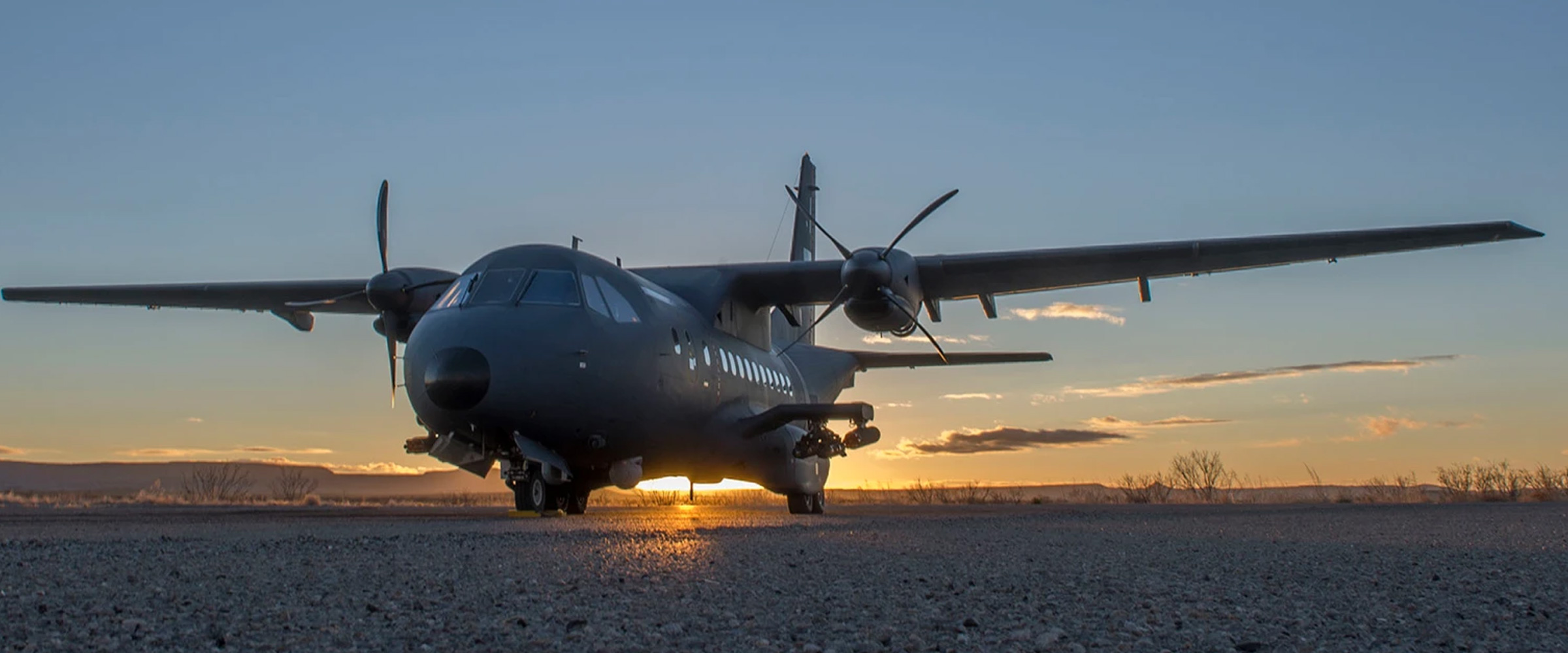 Special Mission Aircraft with sun setting behind it on gravel airstrip