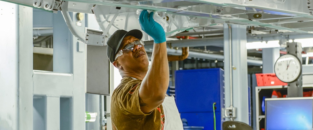 A man wearing gloves, a hat, safety glasses and an apron works on a machine on Northrop Grumman's Integrated Assembly Line