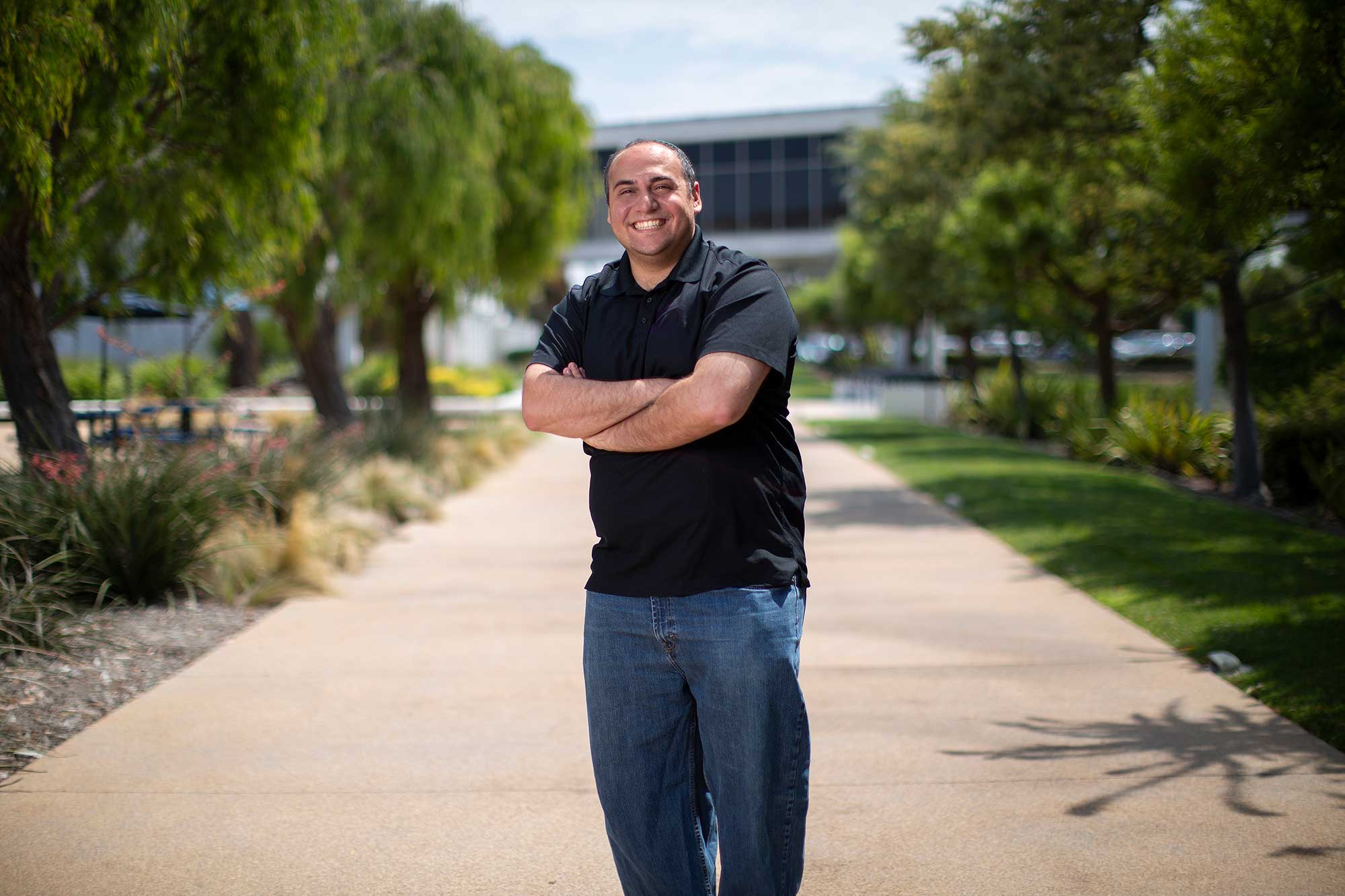 a man stands on a sidewalk and smiles at the camera with his arms crossed