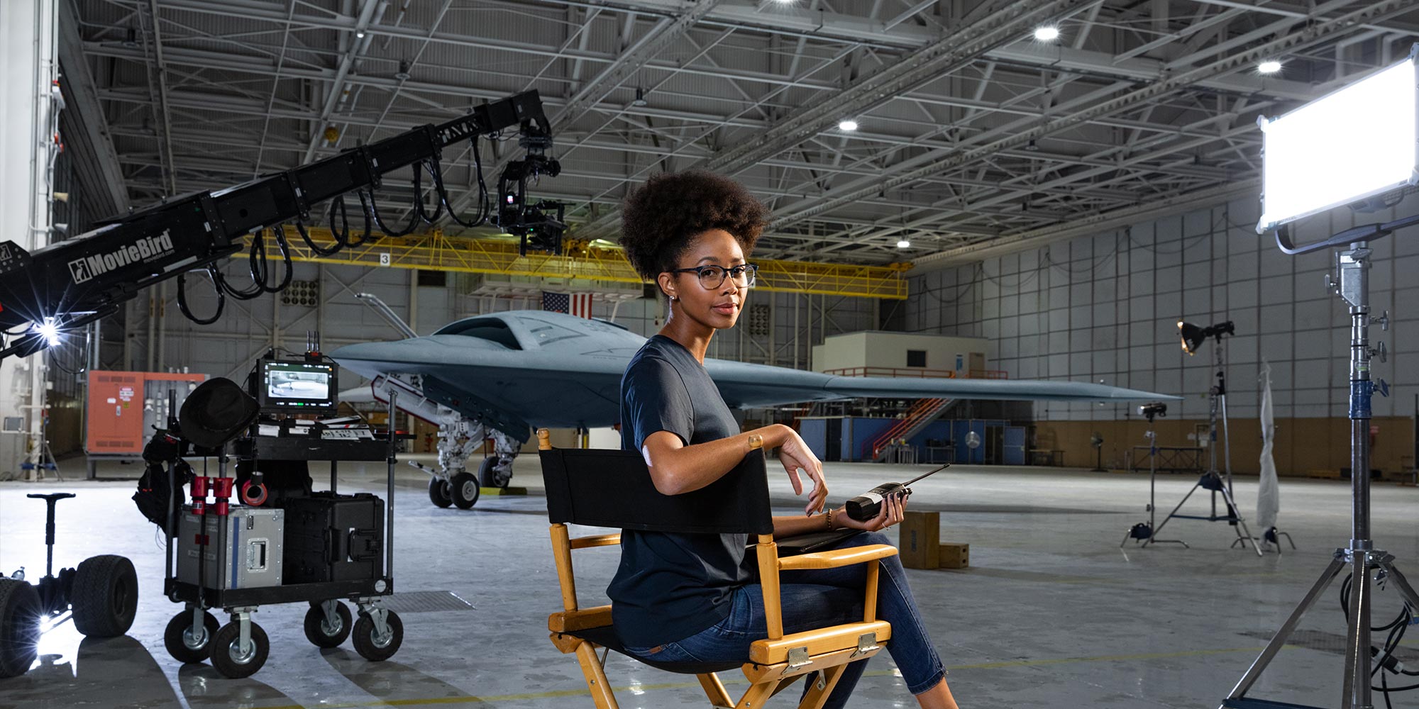 Defining Possible through your Career in Science, Technology and Engineering. young black woman in director's chair in front of B-2 Bomber