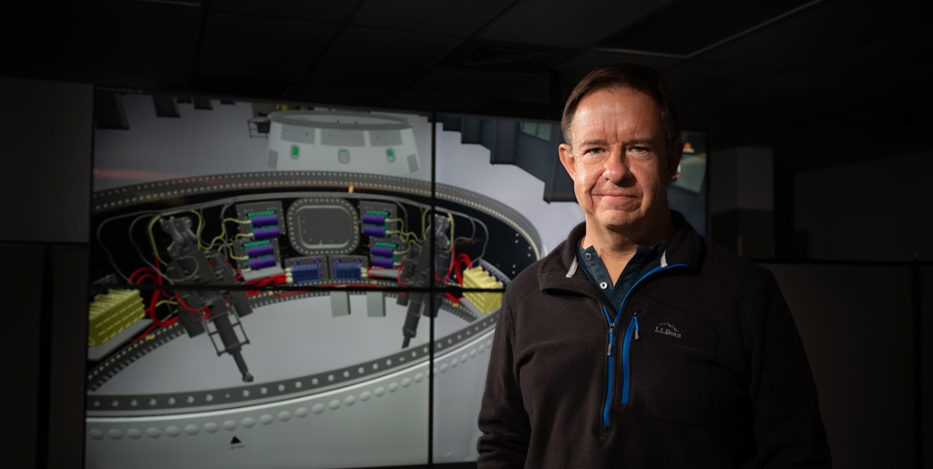 a white man stands in front of a computerized image