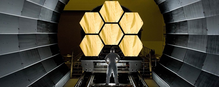 Man standing in a tunnel looking at the gold hexagon mirrors of the James Webb Space Telescope
