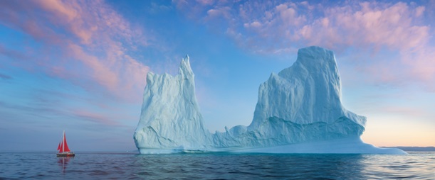 Red sailboat sails by large iceberg.