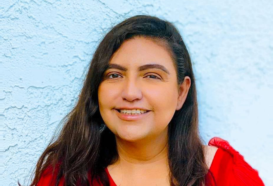 a woman in a red blouse stands against a white wall