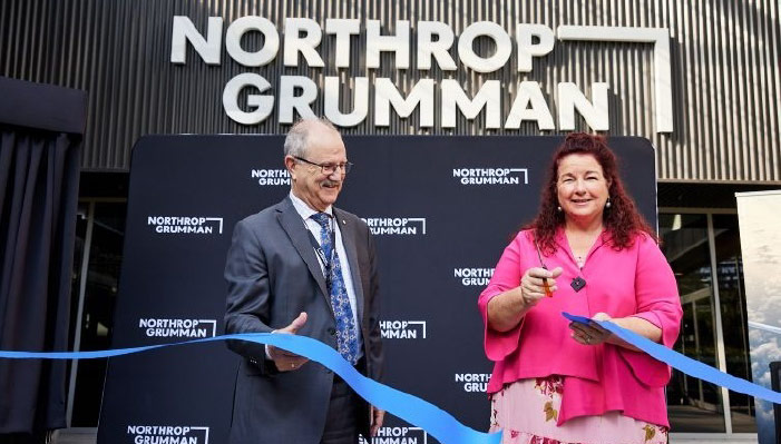 Northrop Grumman Australia Ribbon Cutting A man and woman stand outside a Northrop Grumman office building and cut a blue ribbon