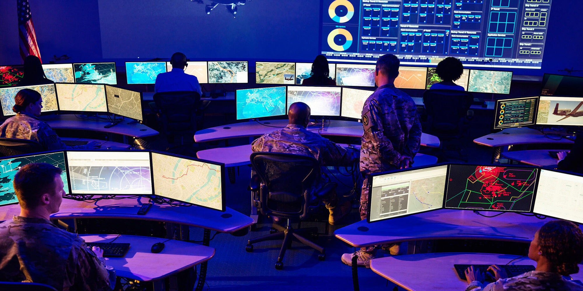 personnel in command center that displays various reports on large monitors