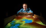 Headshot of man peering over virtual reality sandbox with water and mountains