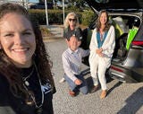 four people in front of a car loaded with donations