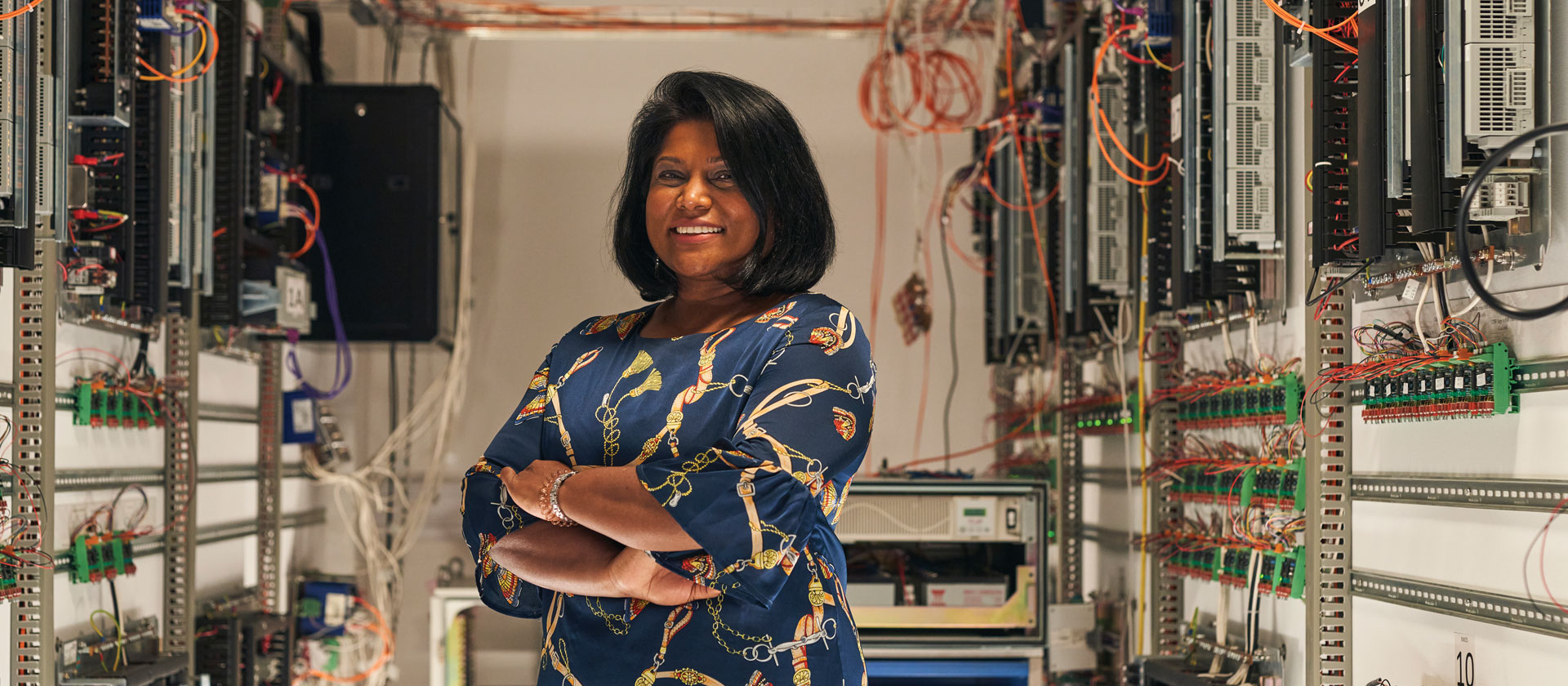 Image of woman with crossed arms looking at viewer in computing server room. 