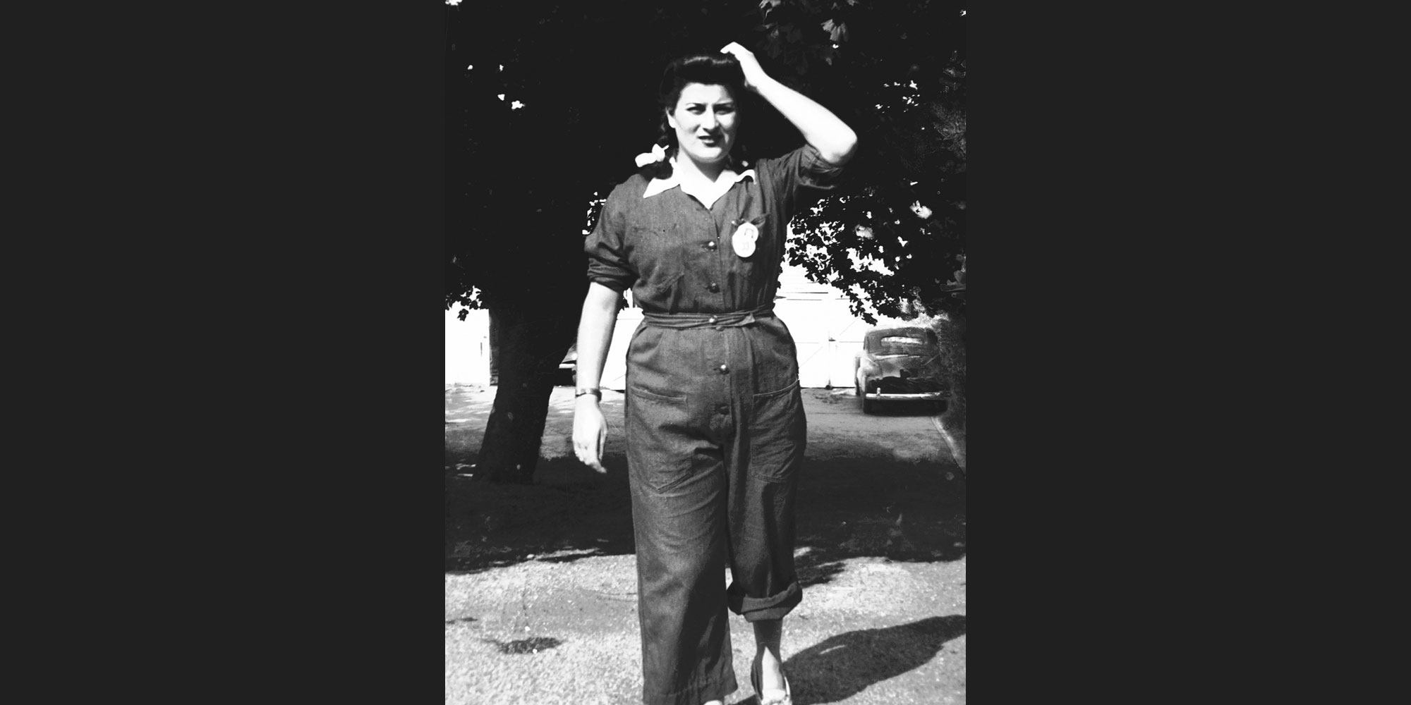 black and white photo of woman walking in the 1940s wearing worker uniform. 
