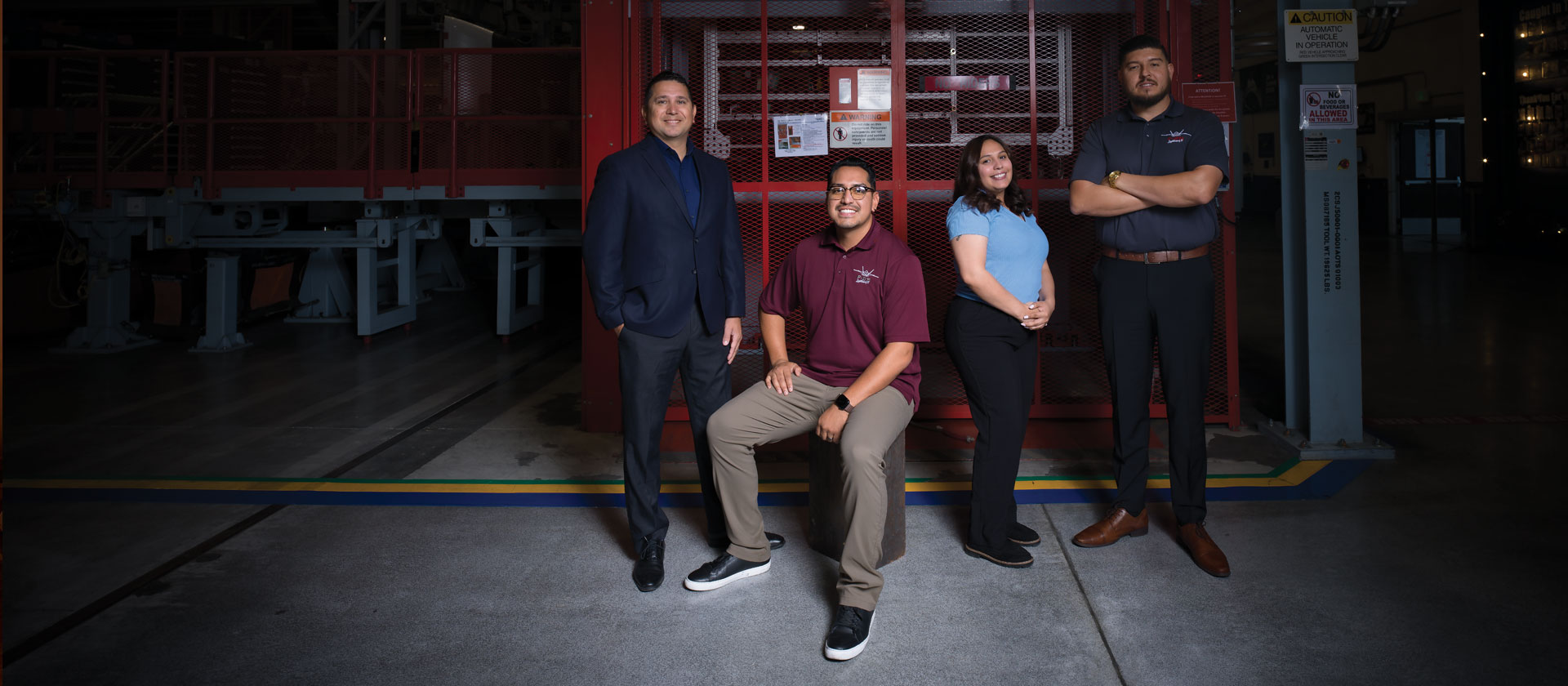 Group of people posing and smiling in manufacturing facility.