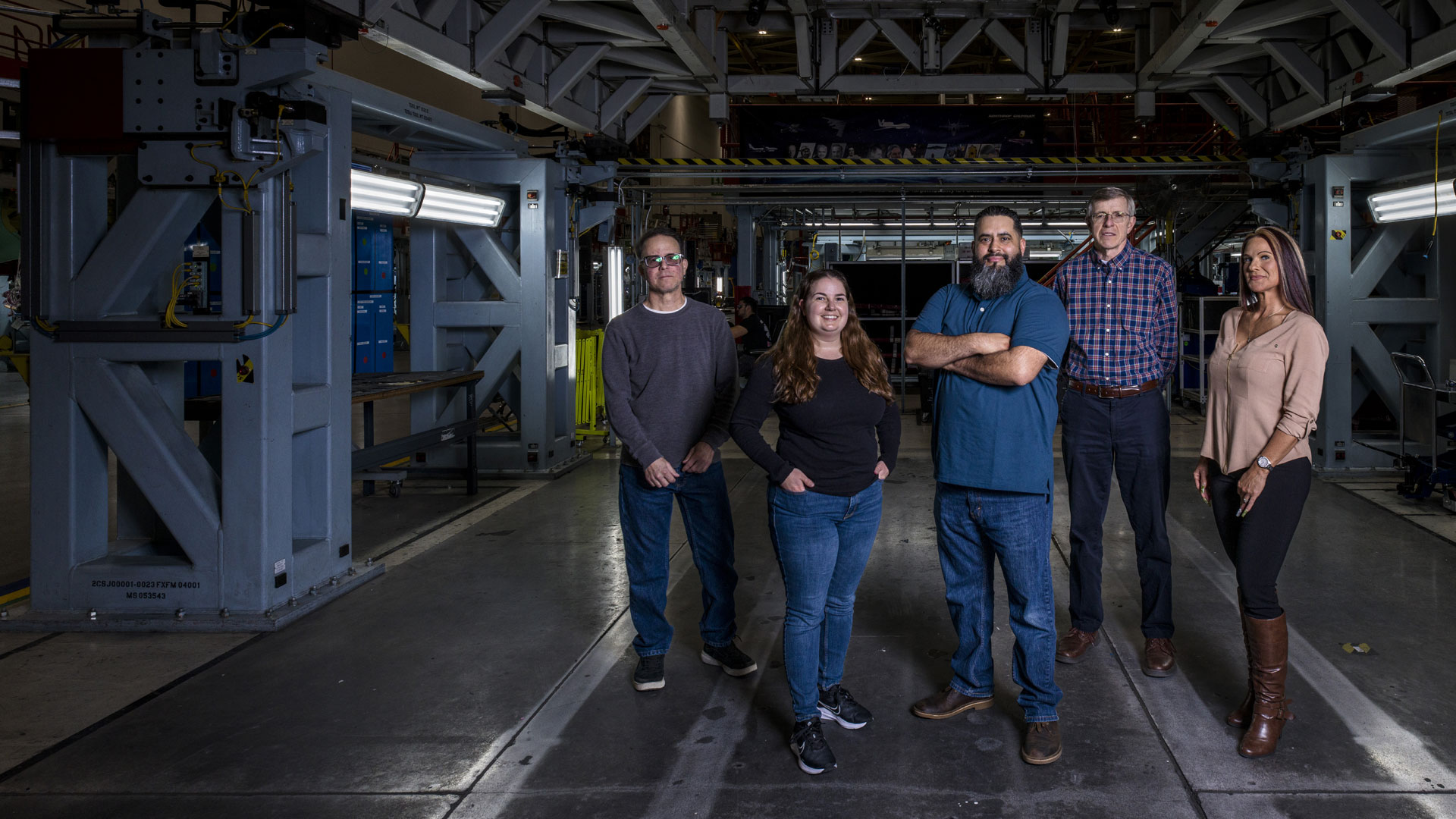 Five employees stand in an industrial space, some sitting or standing on ladders.