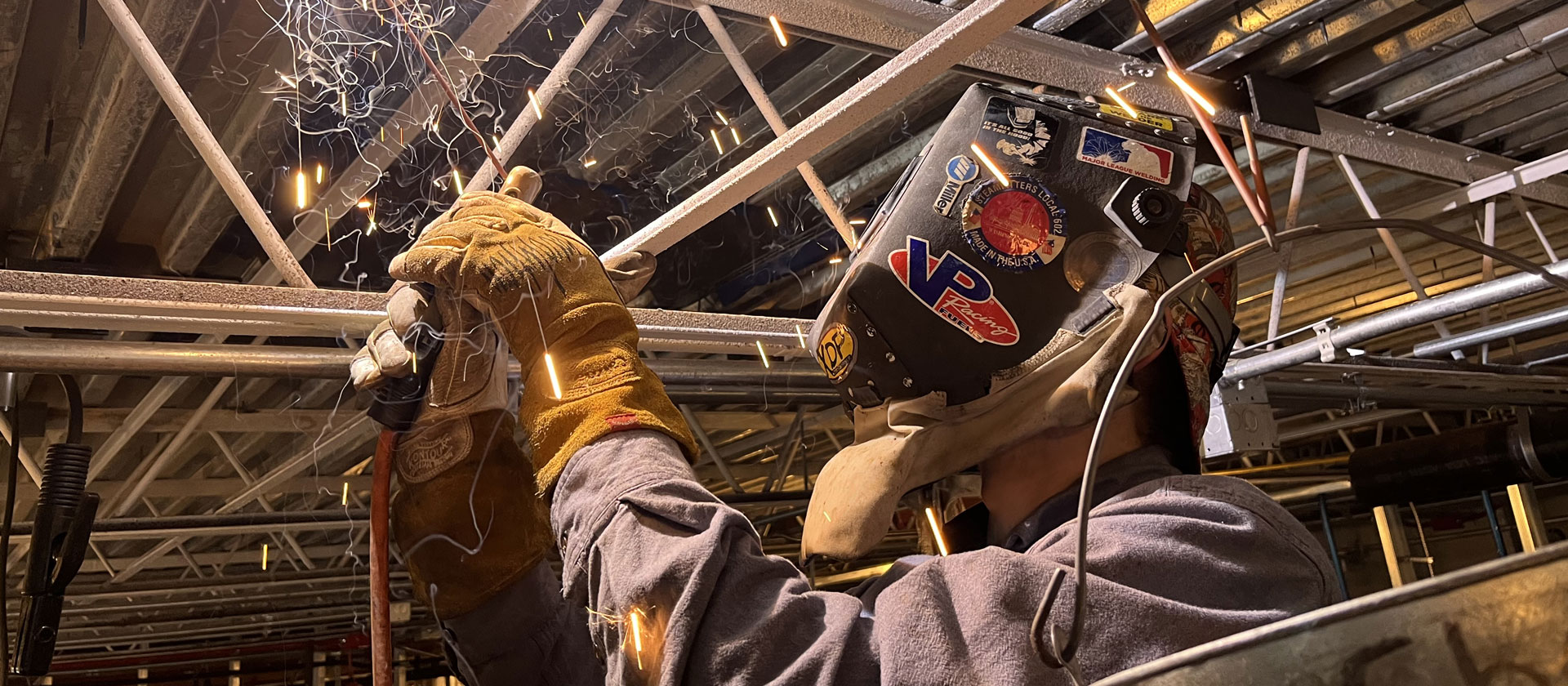 Man with helmet on welding metal with sparks flying.