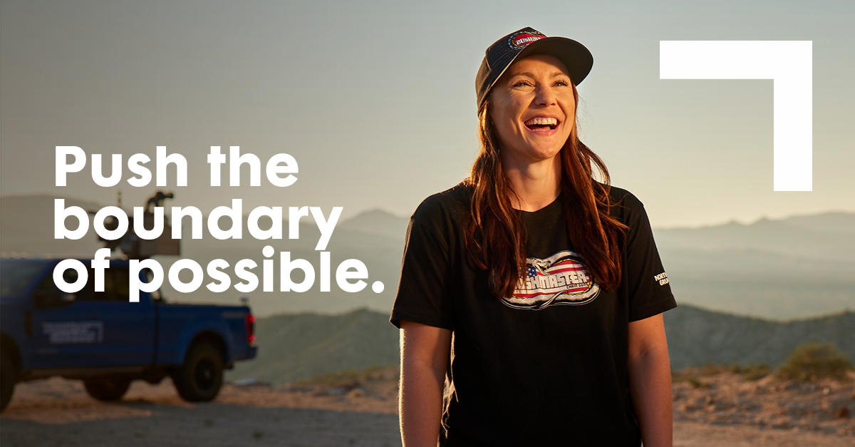 PushTheBoundary_InFeed Female smiling wearing baseball cap standing in front of vehicle