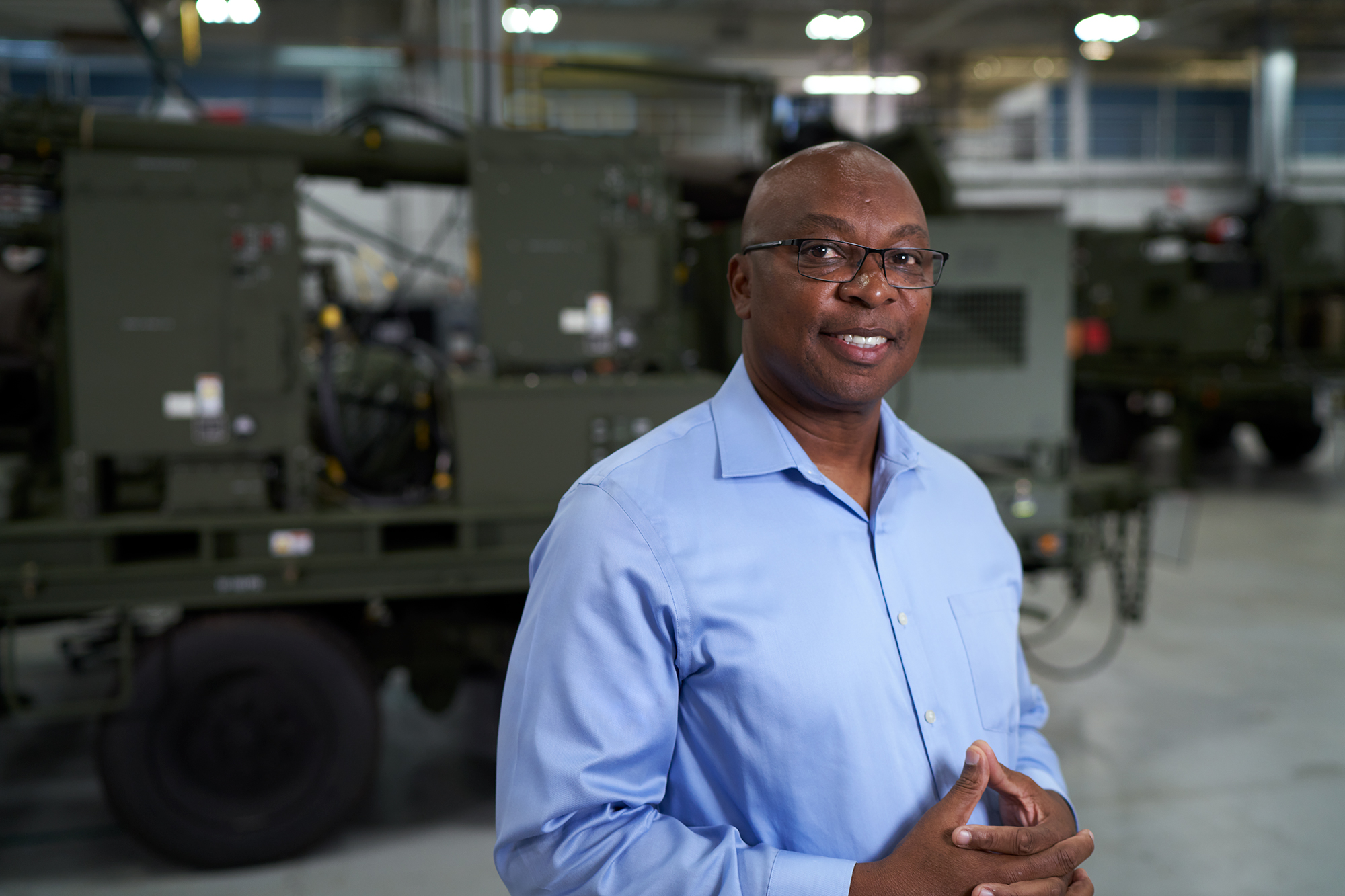 22-1020-RobertMason_059 Smiling Employee with glasses wearing blue shirt standing in front of land equipment
