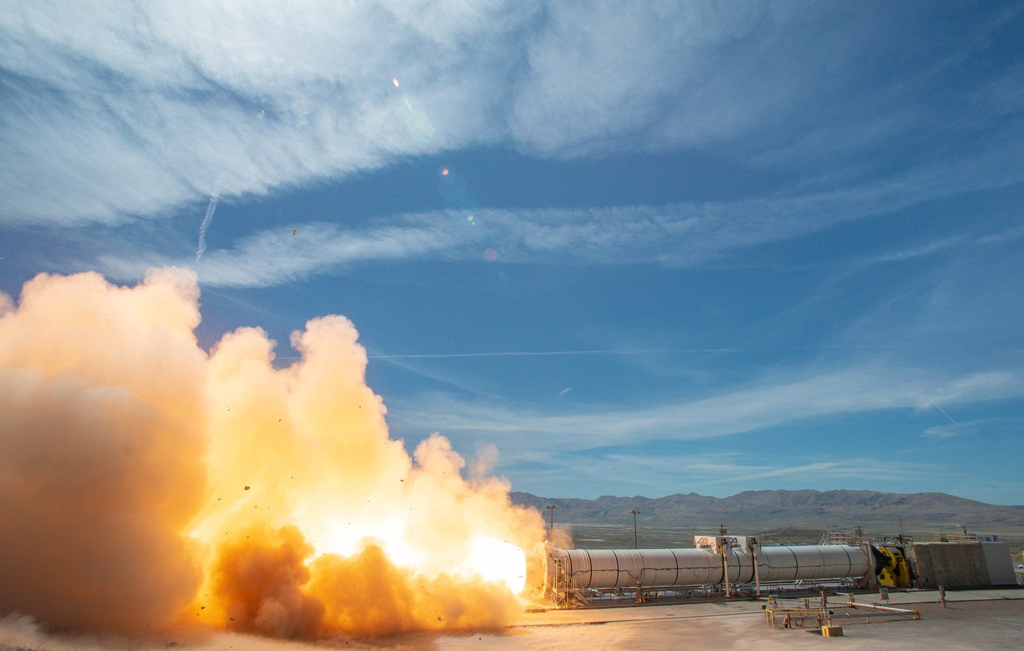 FSB-Web-3 A rocket motor test firing at test site in front of mountains and blue sky