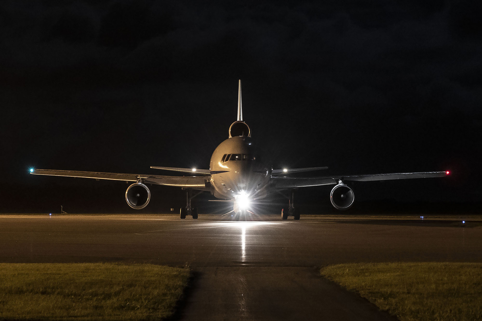 Front view of airplane with bright headlight on runway in front of night sky readying for takeoff
