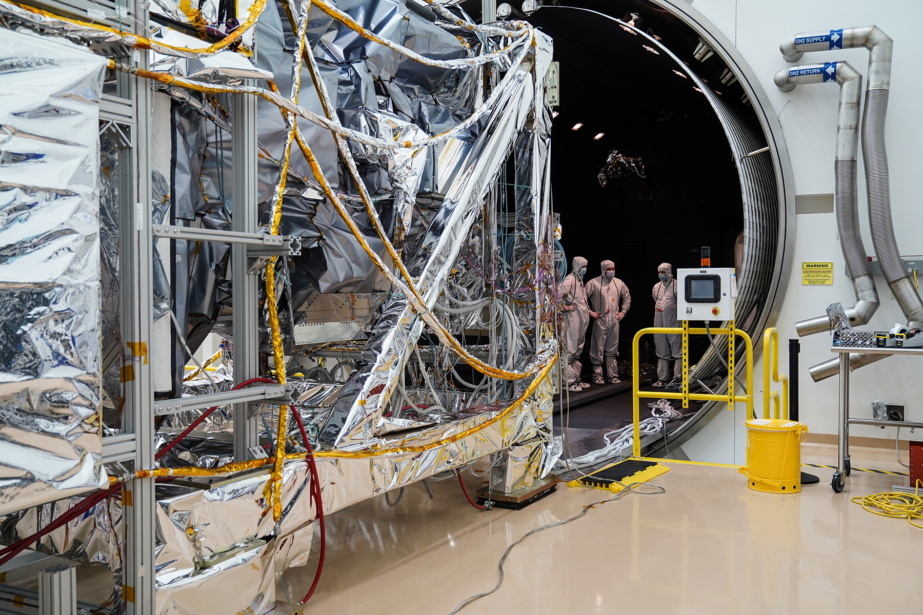 A satellite and engineers in a thermal vacumm testing facility
