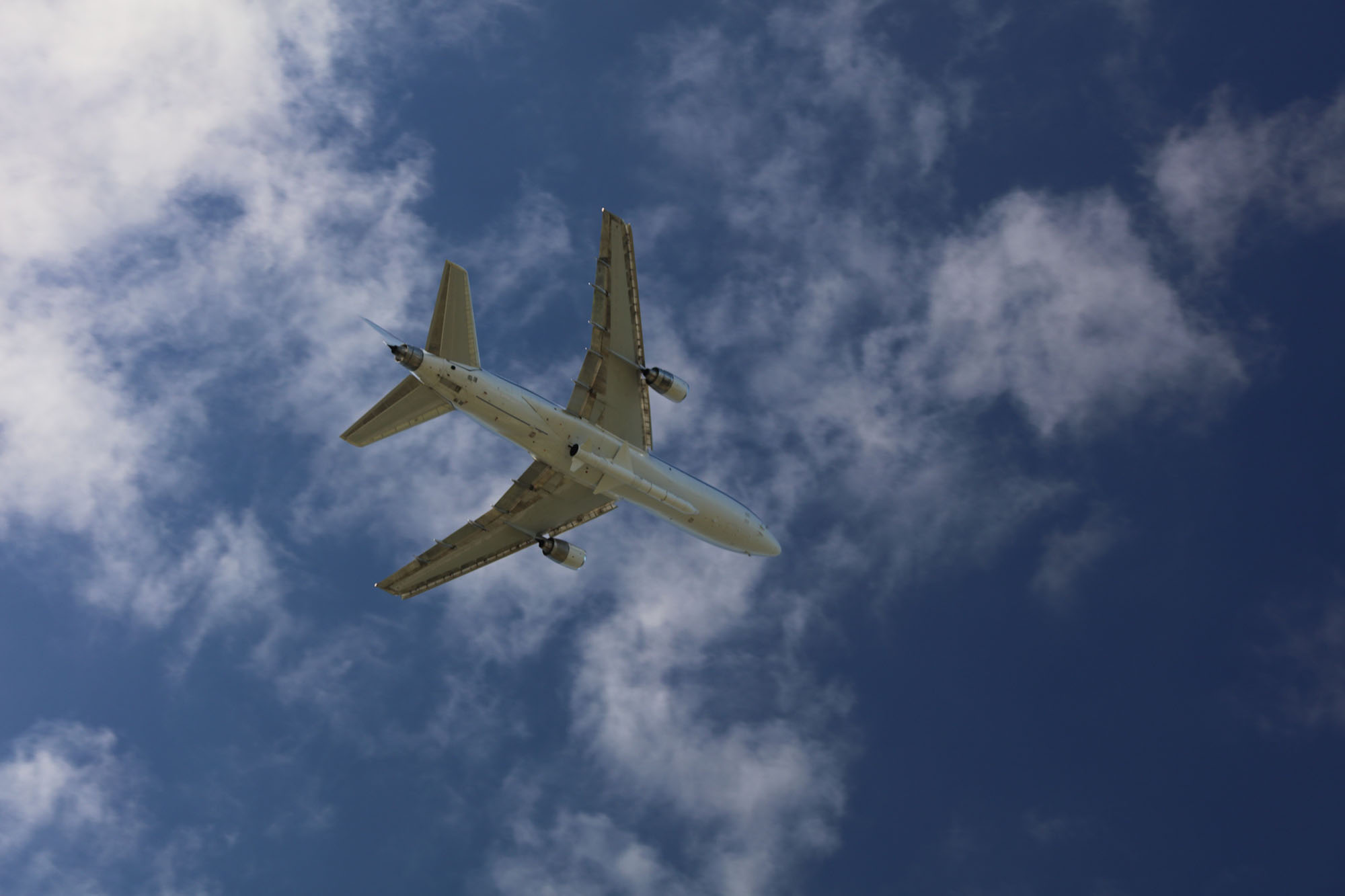 View from ground of the belly of an airplane carrying a rocket in a blue sky with light clouds